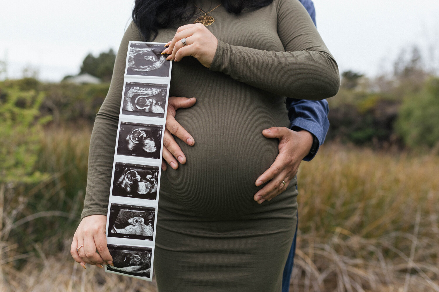  Pregnant couple posing with ultra sound photos against field background 
