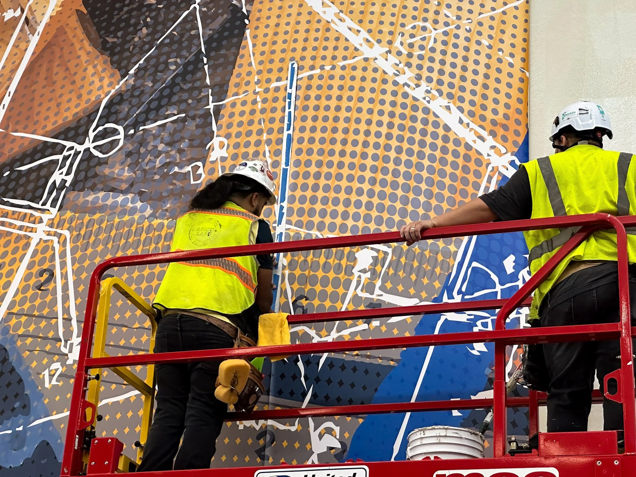 Installers on a lift applying a large colorful vinyl wall mural to a commercial building in Houston.