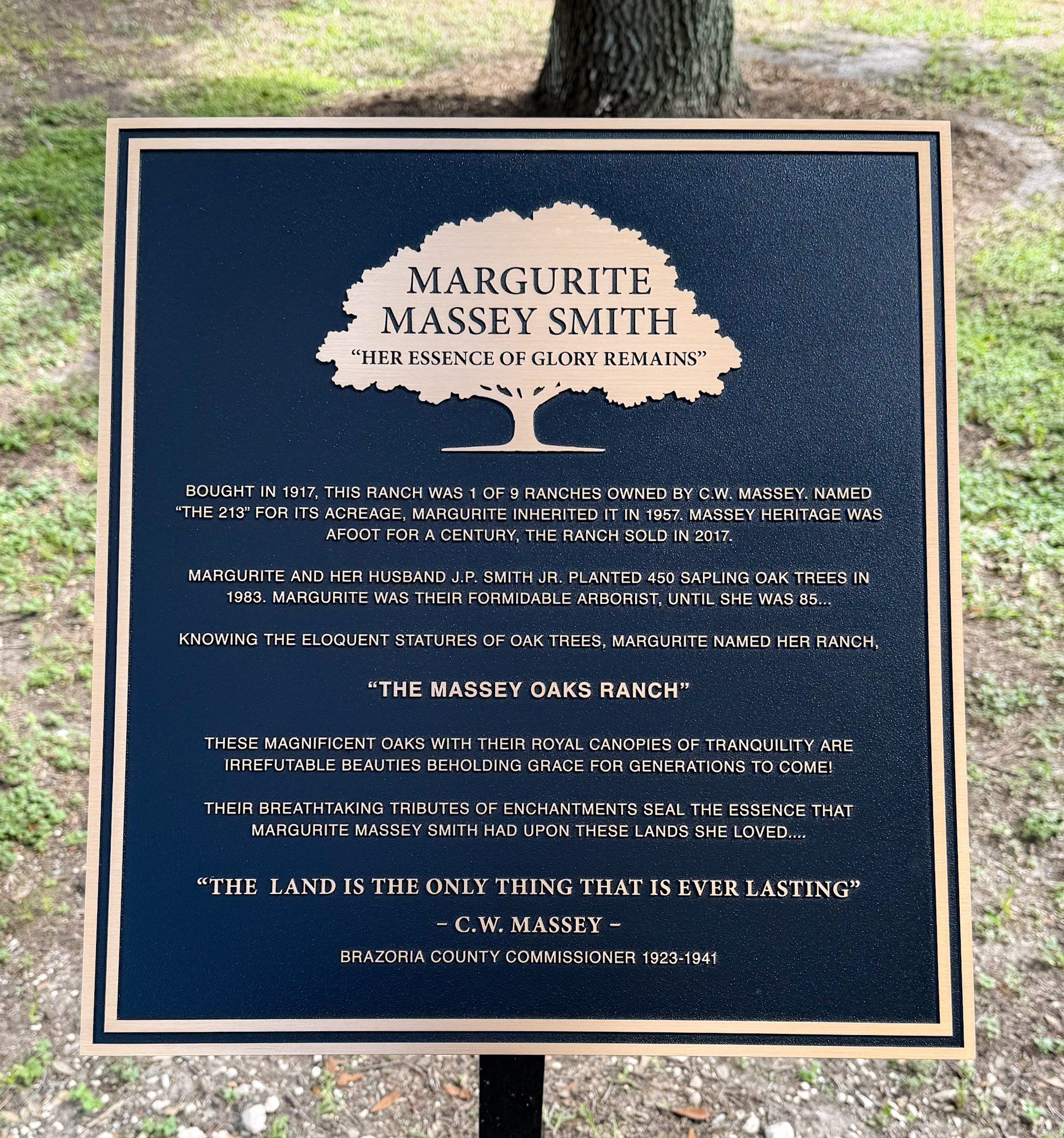 Outdoor bronze memorial plaque honoring Margurite Massey Smith with raised lettering and tree artwork mounted on a post.
