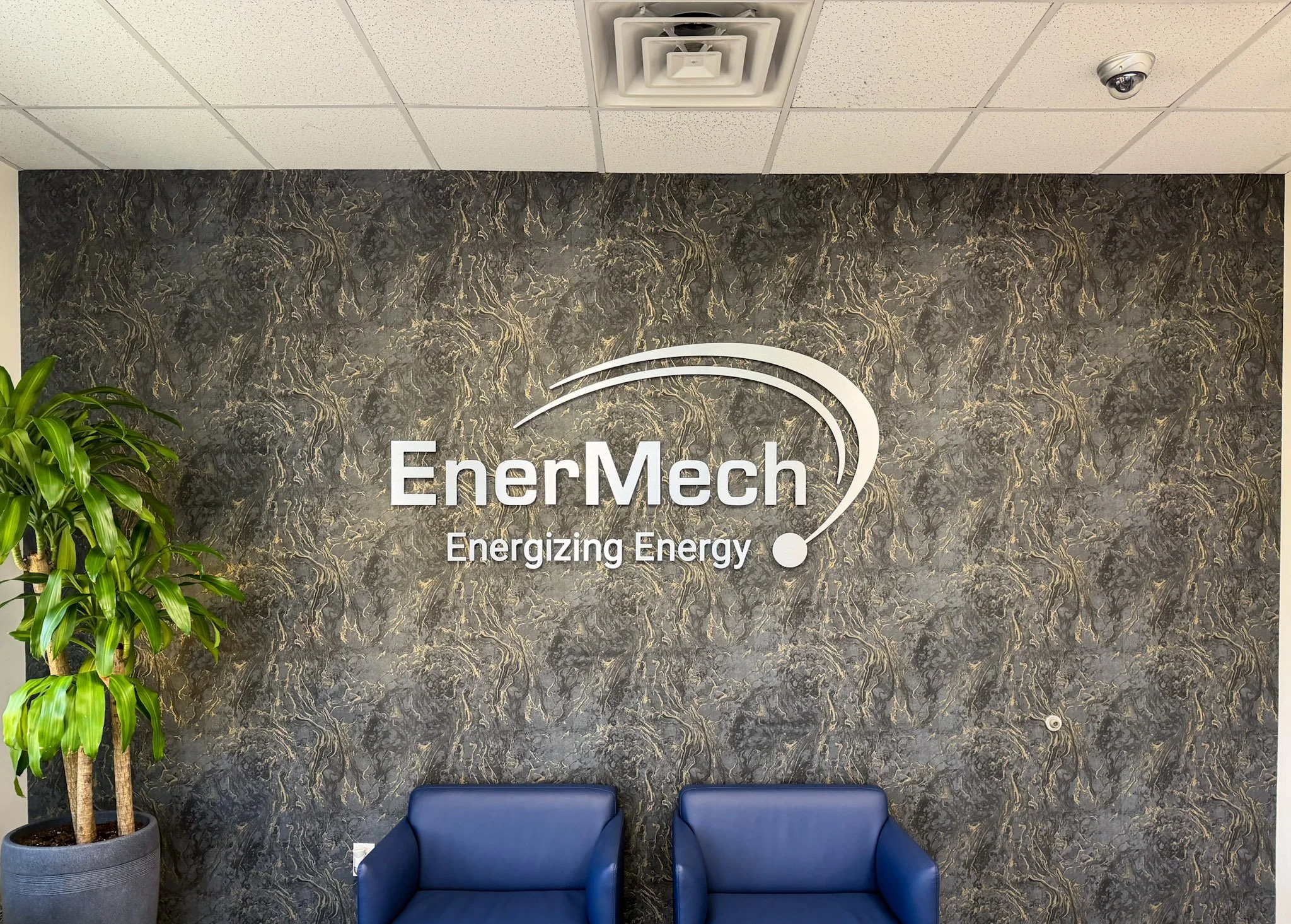 Brushed metal dimensional lobby logo sign installed on a decorative feature wall in a corporate office reception area.