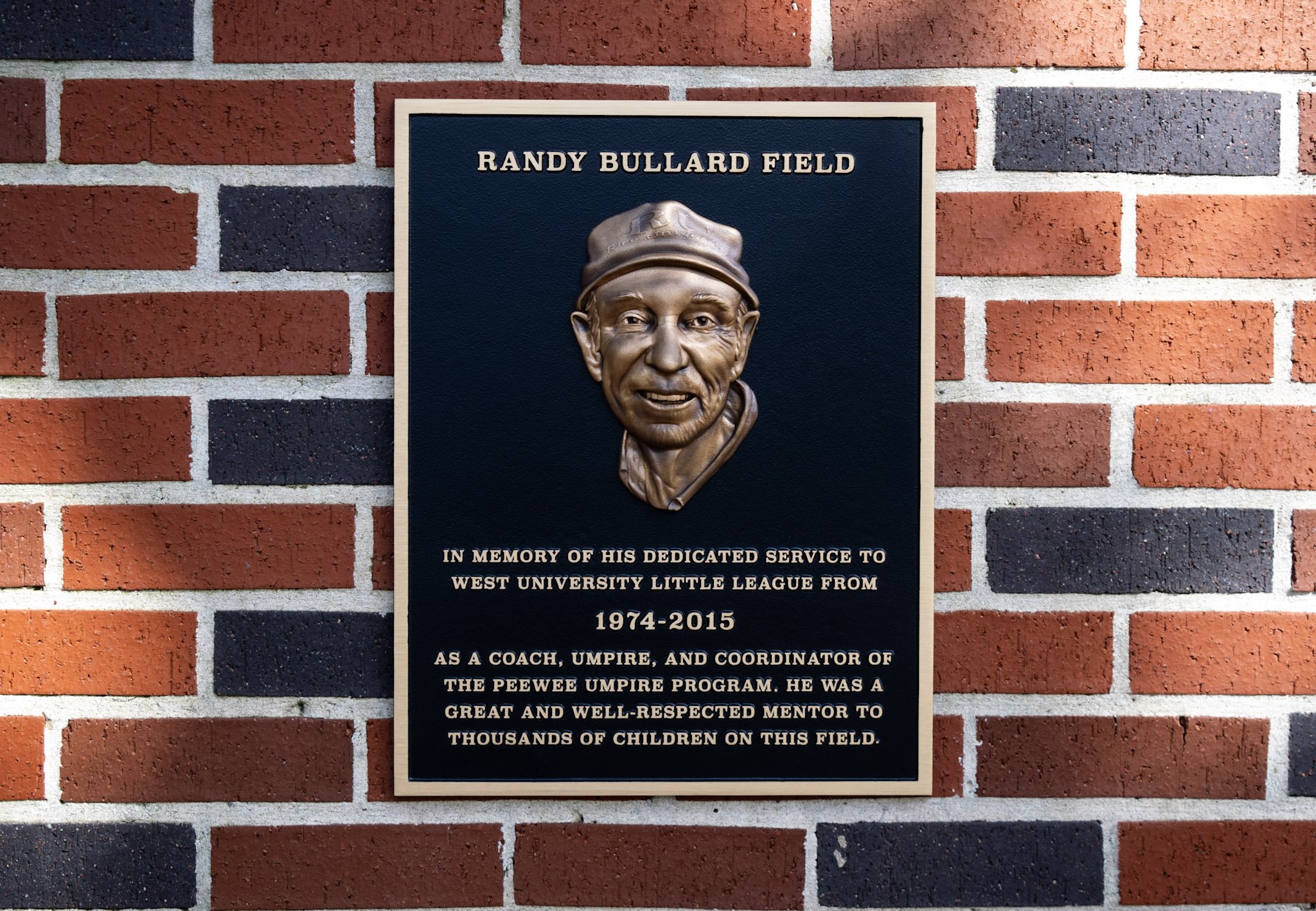 Bronze bas-relief memorial plaque for Randy Bullard Field with a sculpted portrait and raised dedication text mounted on brick.
