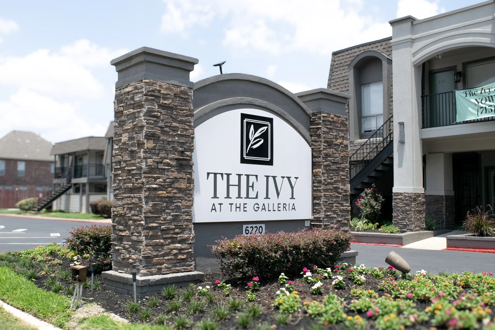 Stone monument sign at an apartment community entrance with dimensional lettering, masonry columns, and landscaped outdoor signage.