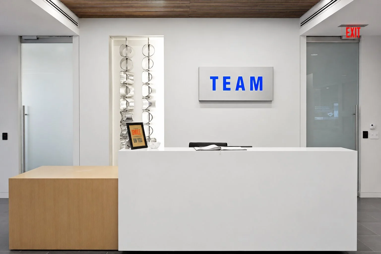 Backlit dimensional lobby logo sign mounted on a brushed metal panel behind a modern corporate reception desk.