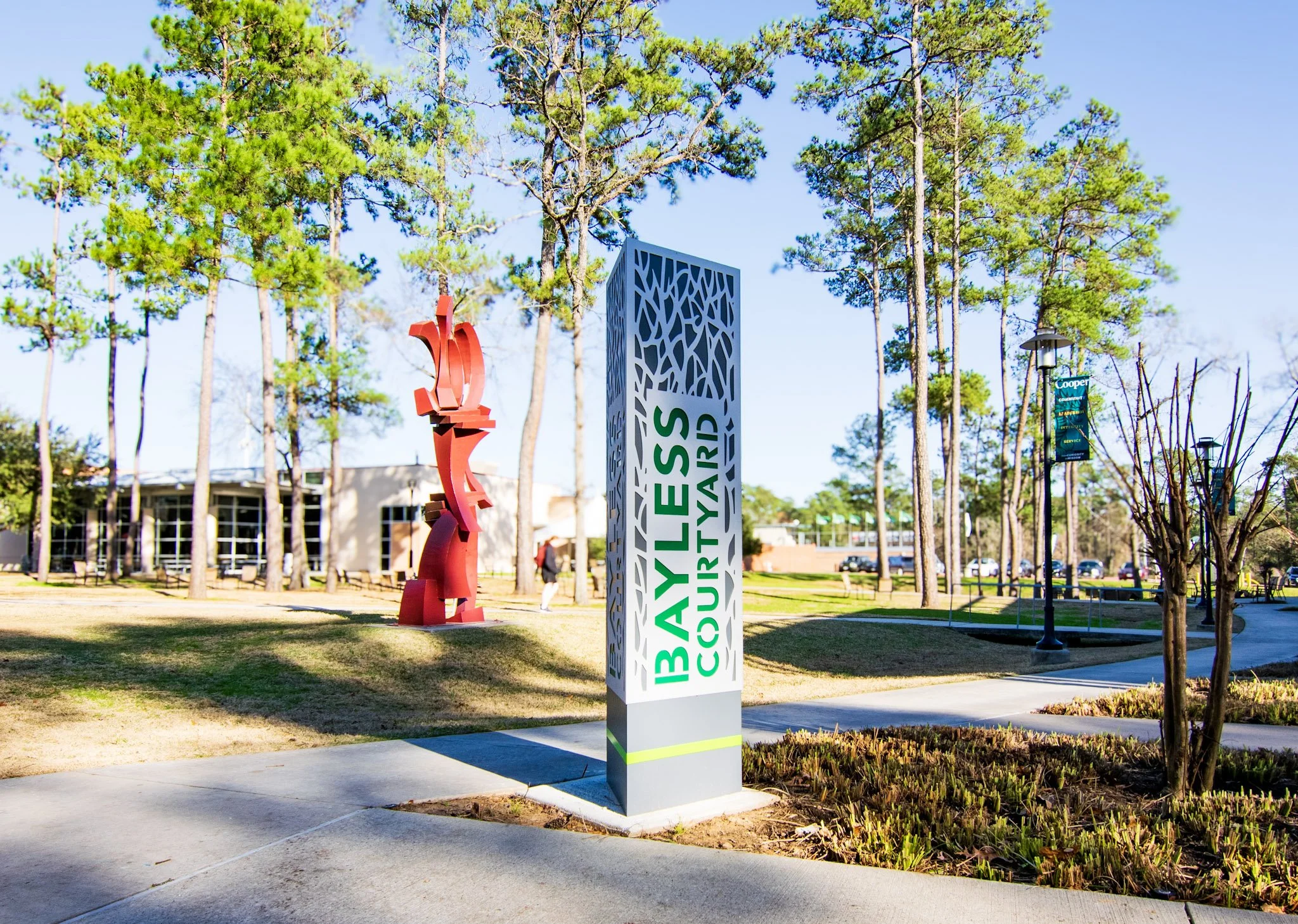 Custom monument sign with dimensional lettering and decorative metal panels installed along a campus walkway, providing outdoor wayfinding and property identification.
