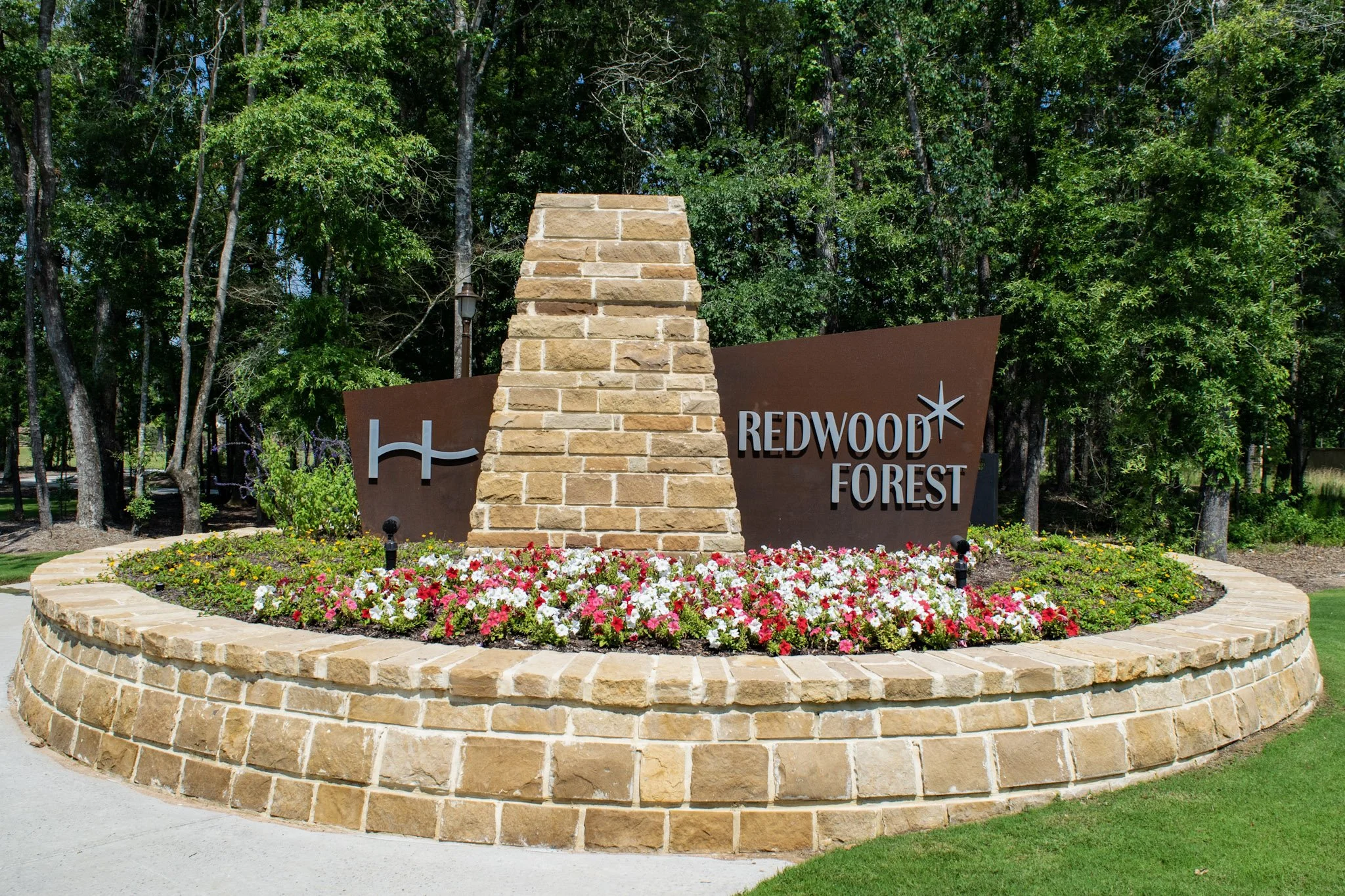Stone monument sign with metal lettering installed at the Redwood Forest community entrance, surrounded by landscaped flower beds and decorative masonry.