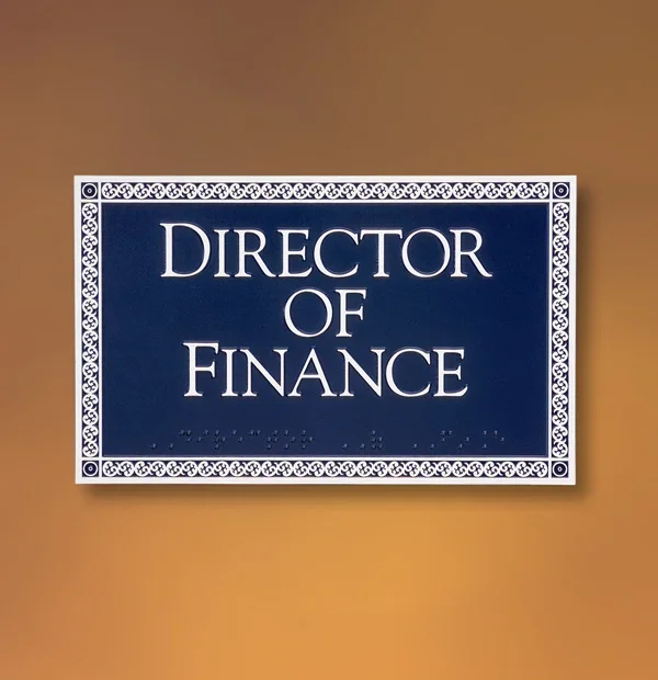 Decorative ADA office sign in Houston reading “Director of Finance” with raised white lettering on a deep blue plaque and intricate patterned border.