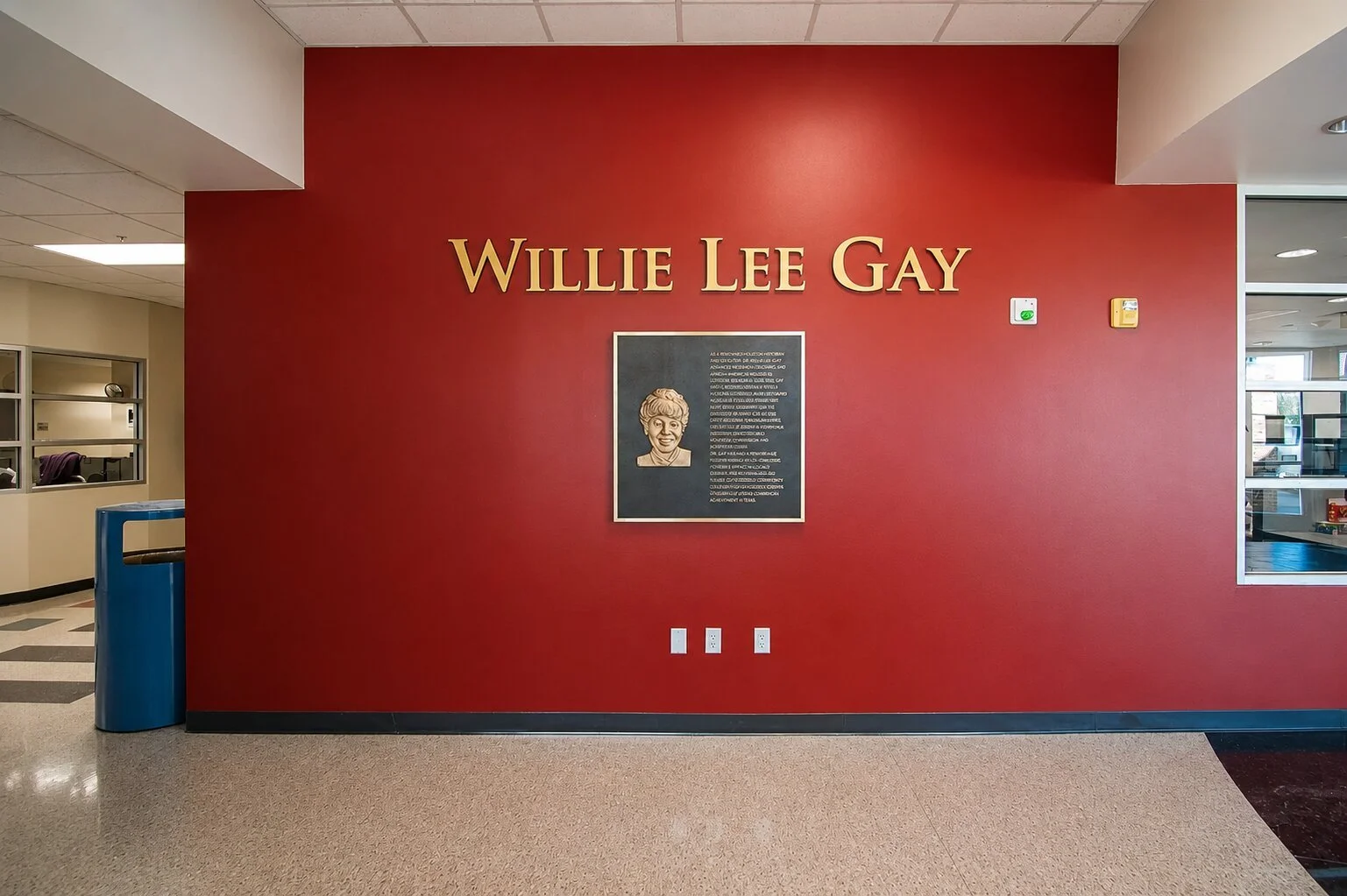 Bronze recognition plaque with portrait and dimensional lettering honoring Willie Lee Gay on a red wall at Houston Community College.