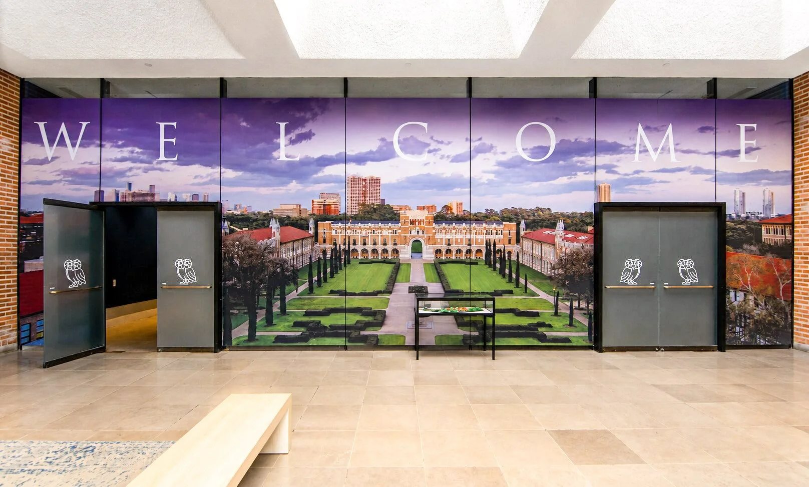 Large custom wall mural installed by Saifee Signs in the Rice University lobby, featuring a campus welcome graphic with panoramic campus imagery and branded entrance doors.