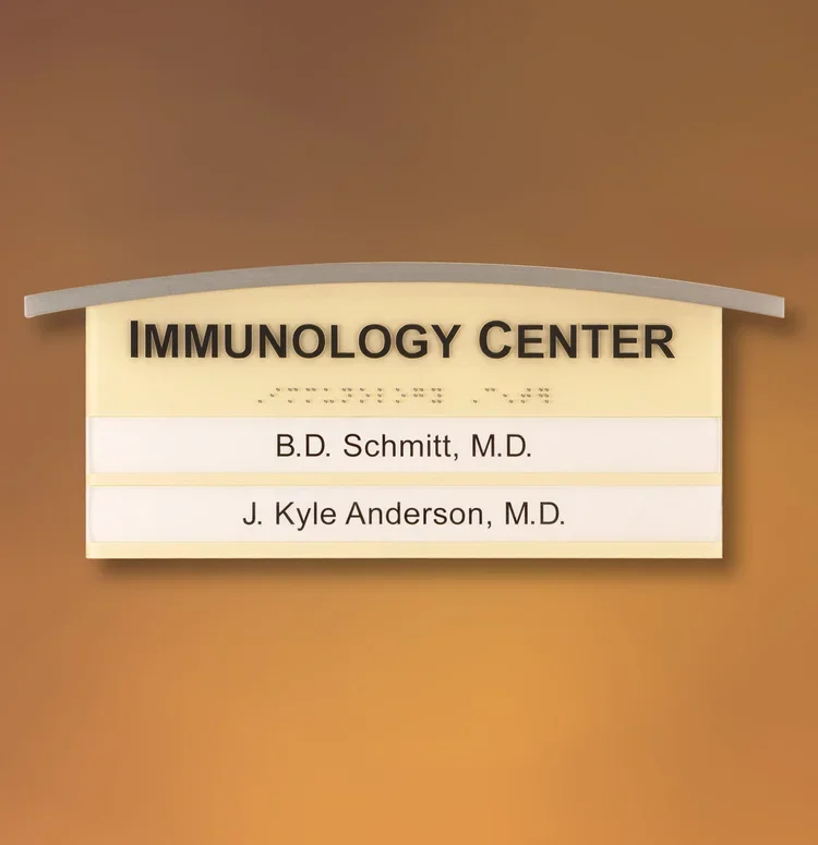 Standard ADA immunology center sign with raised tactile lettering and Braille listing physicians’ names, Houston medical facility.