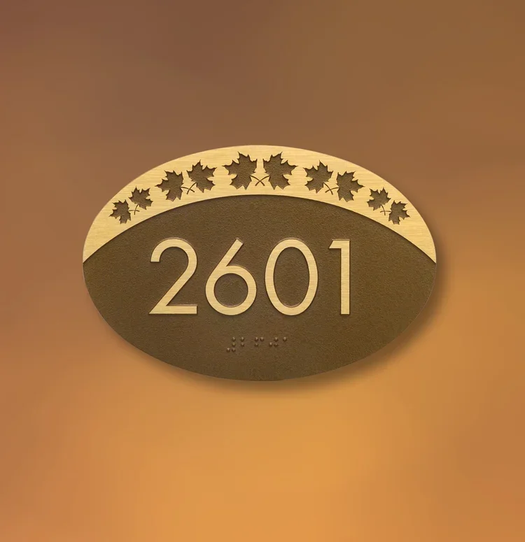 Metal-toned oval ADA room sign with raised number 2601 and leaf border design, stylish textured finish, ideal for offices in Houston.