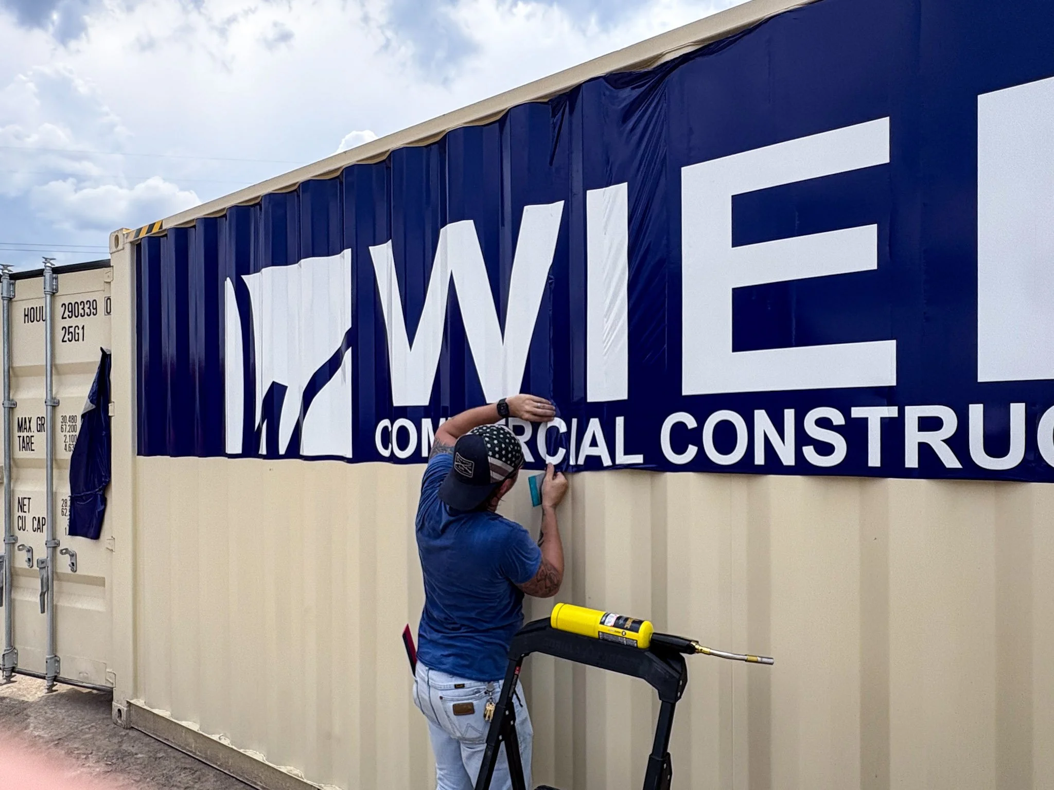 Installer applying large WIER Commercial Construction vinyl graphics to the side of a shipping container.