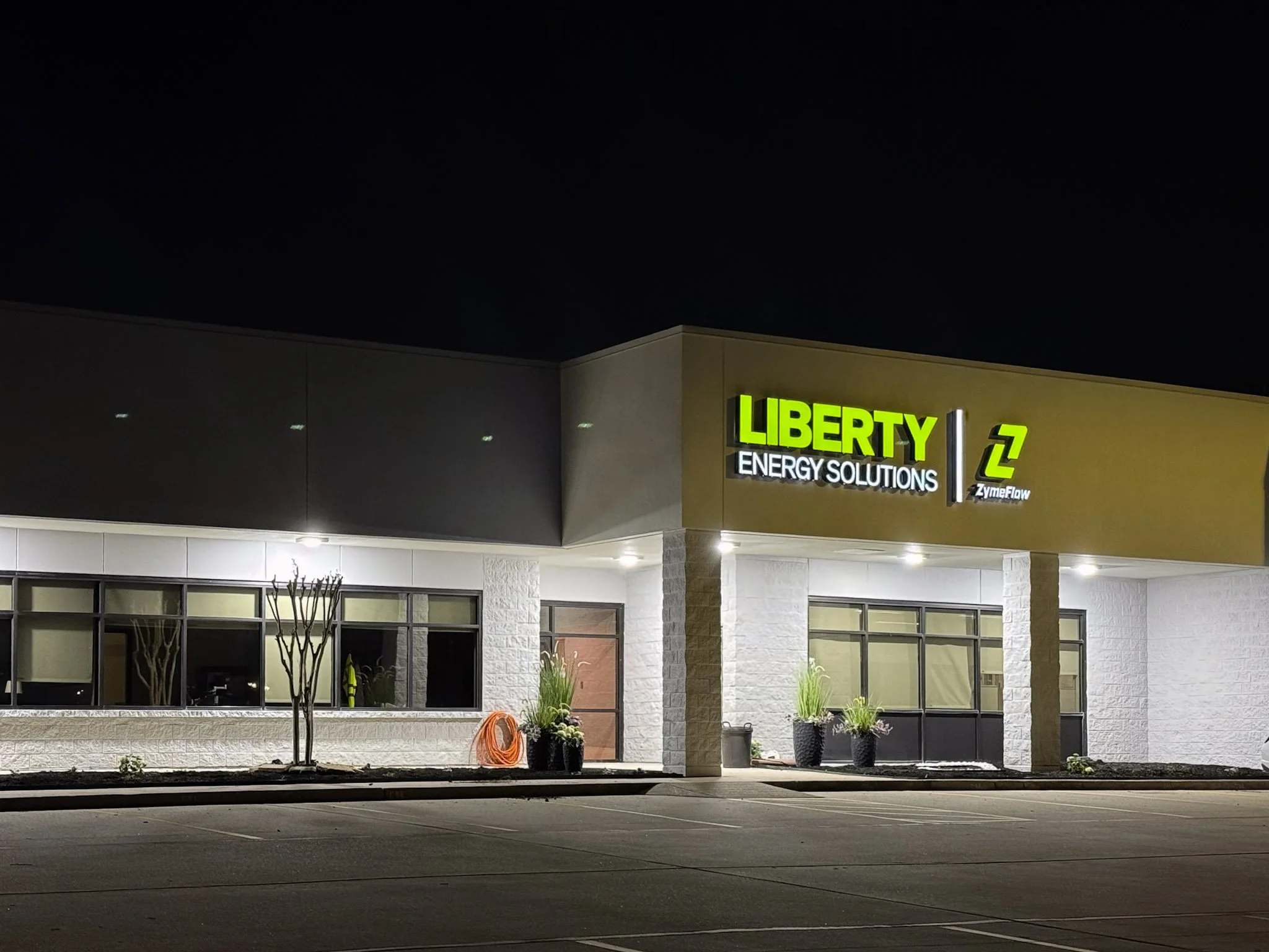 Illuminated Liberty Energy Solutions and ZymeFlow exterior building signs installed on a commercial facility in Houston at night.