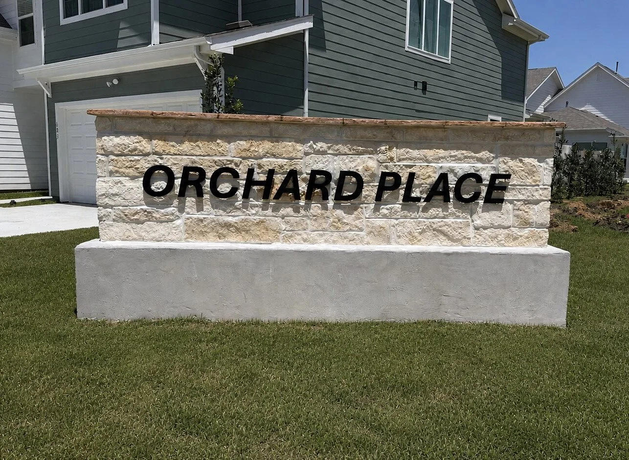 Stone monument sign with black dimensional letters reading Orchard Place at the entrance to a residential community.