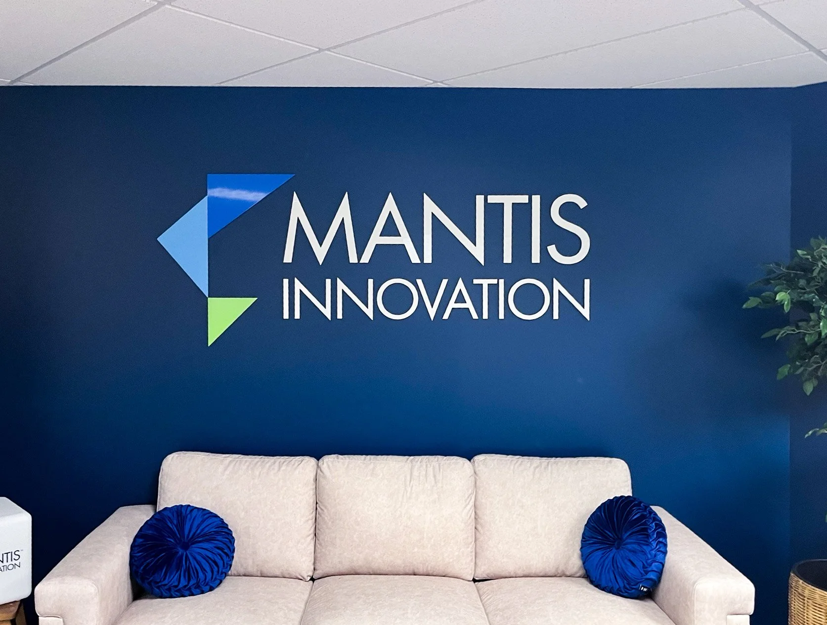 Dimensional office logo sign mounted on a painted feature wall above a reception seating area in a corporate office lobby.