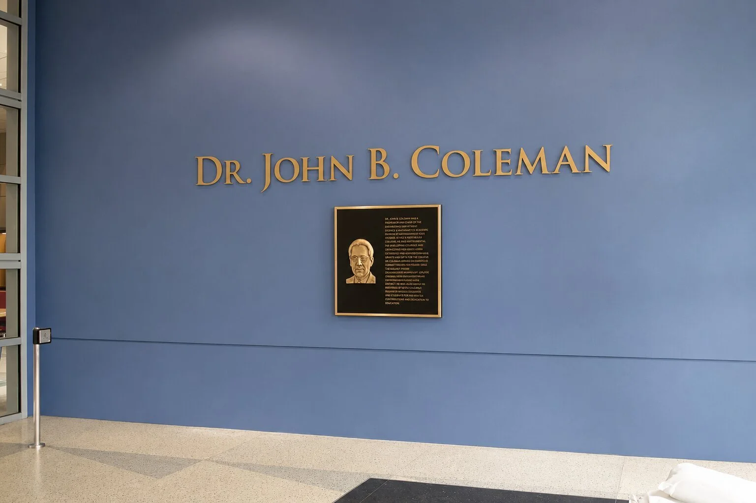 Bronze recognition plaque with portrait and dimensional letters honoring Dr. John B. Coleman on a blue wall at Houston Community College.