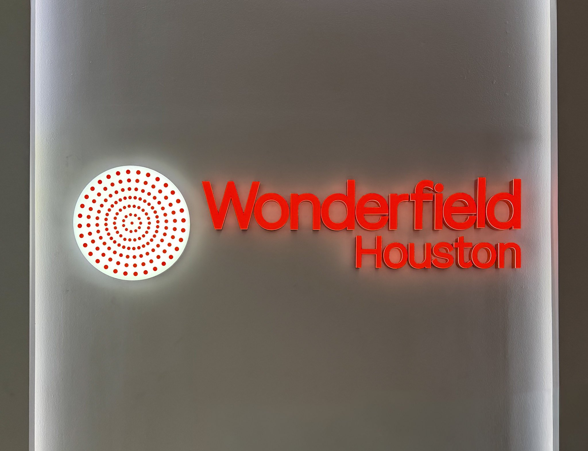 Illuminated acrylic lobby logo sign with halo lighting mounted on a feature wall in a modern corporate office reception area.
