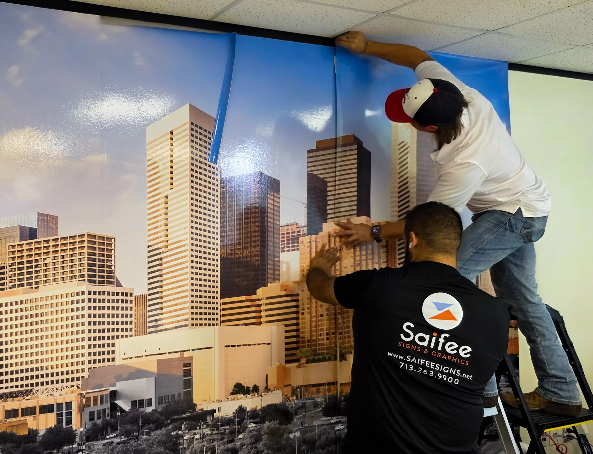 Saifee Signs installers applying a large Houston skyline wall graphic inside a commercial office.