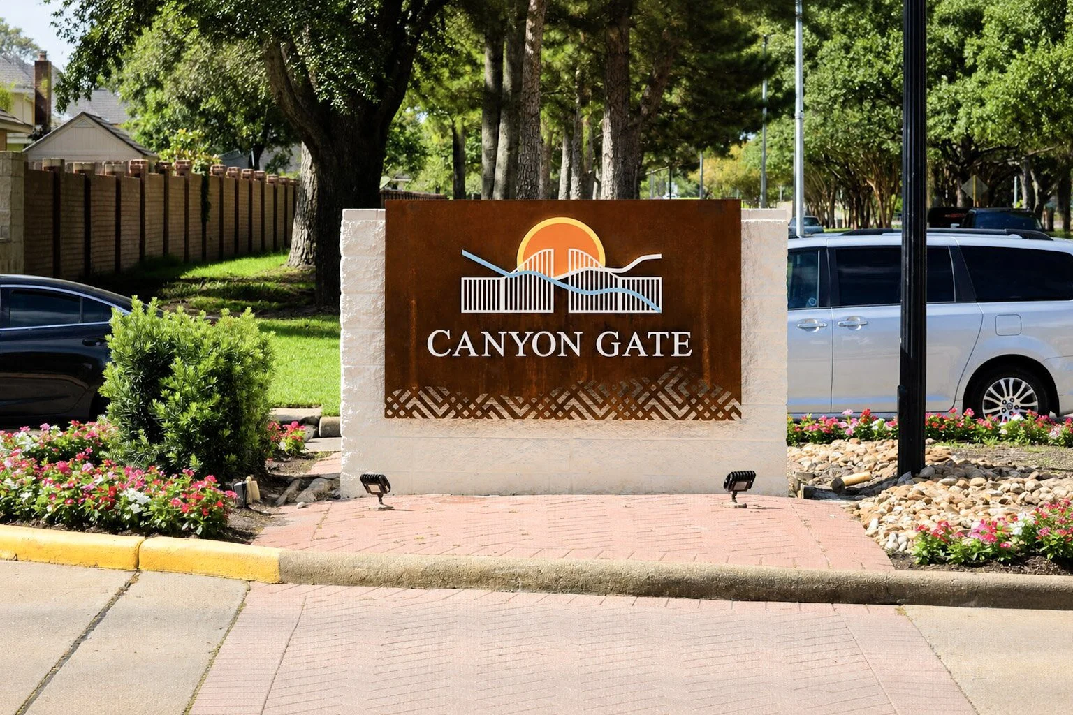 Custom metal monument sign installed at the Canyon Gate community entrance with decorative metal panels, masonry base, and landscaped surroundings.