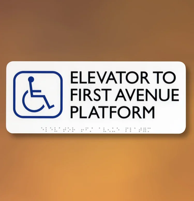 Standard ADA directional sign indicating elevator to First Avenue platform with wheelchair symbol and Braille, located in Houston.