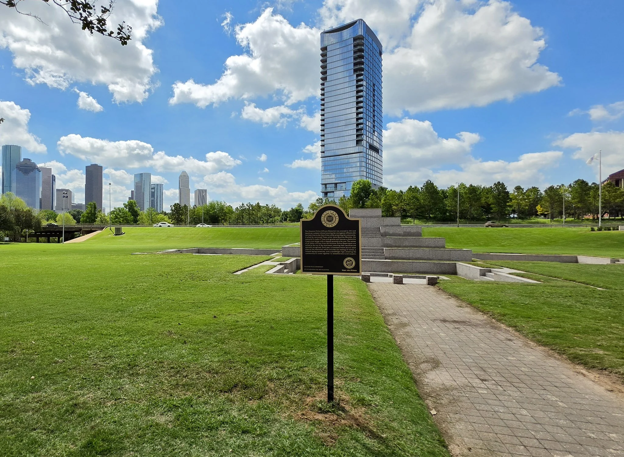 Outdoor commemorative plaque at the Houston Police Officers Memorial with downtown Houston buildings visible in the background.