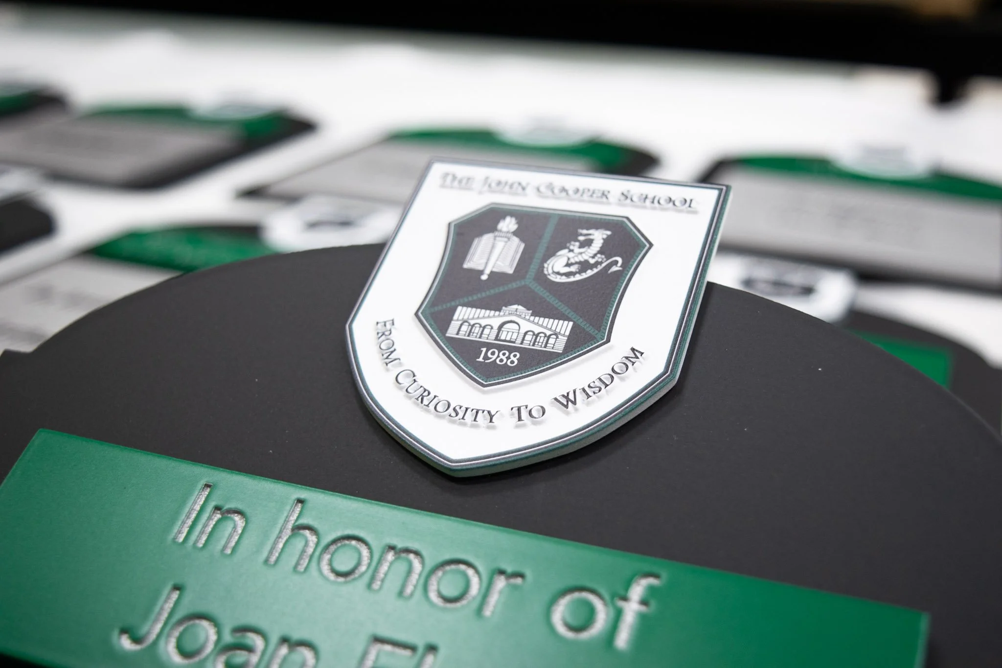 Custom recognition plaques for The John Cooper School featuring the school crest, green accents, and engraved memorial lettering.