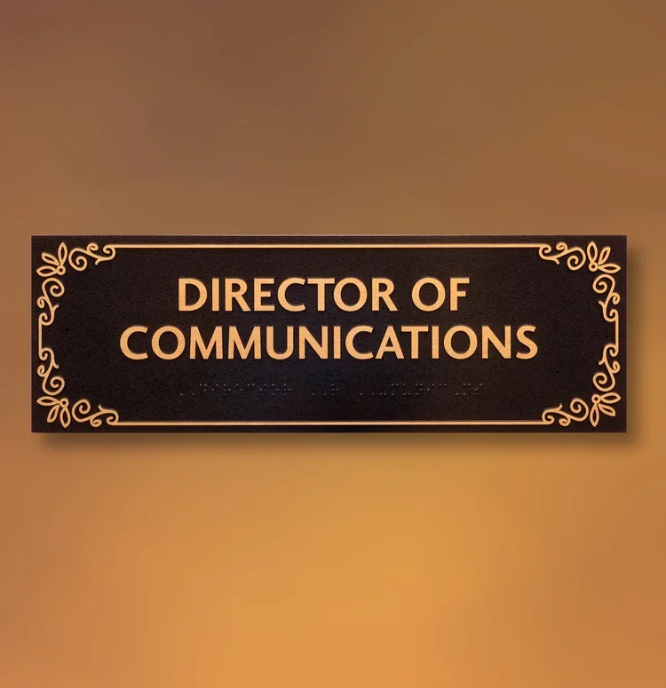 Metal ADA title sign reading Director of Communications with decorative corners, tactile lettering and braille, premium finish for Houston offices.