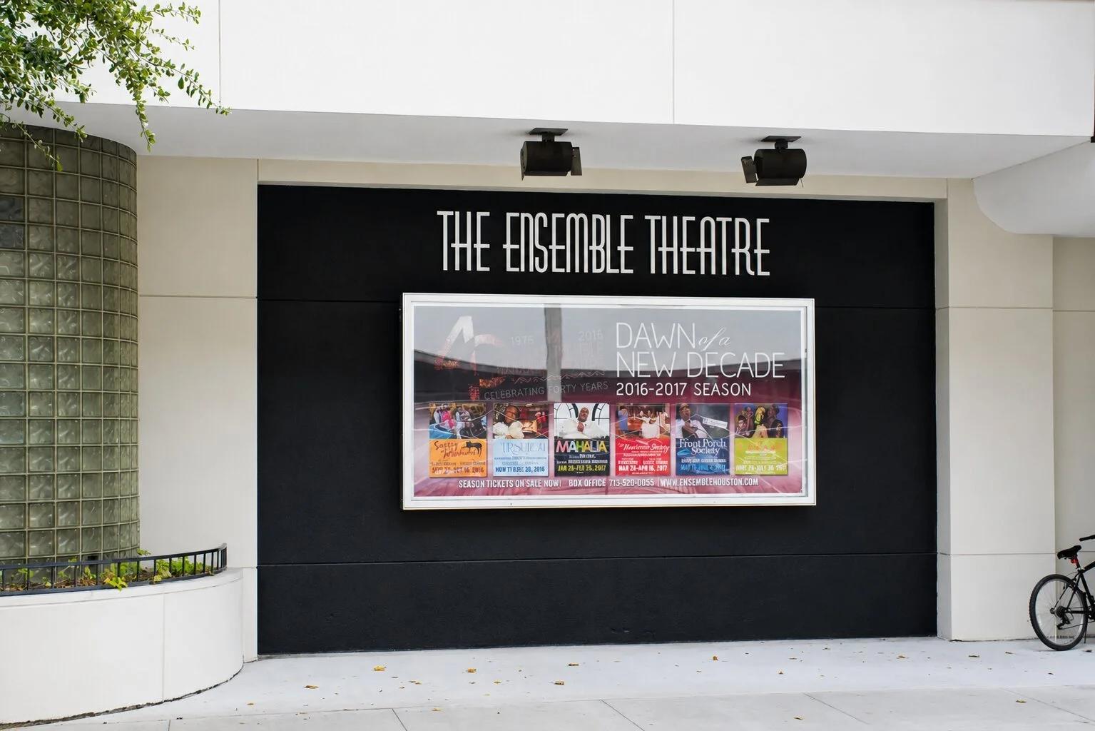 The Ensemble Theatre in Houston with exterior wall lettering above a framed season display on a black accent wall near the building entrance.
