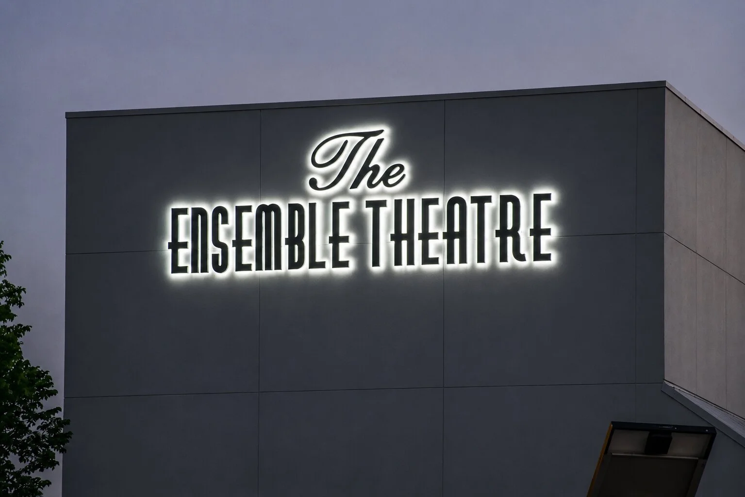 Illuminated The Ensemble Theatre exterior sign in Houston with halo-lit dimensional letters mounted high on the building facade at dusk.