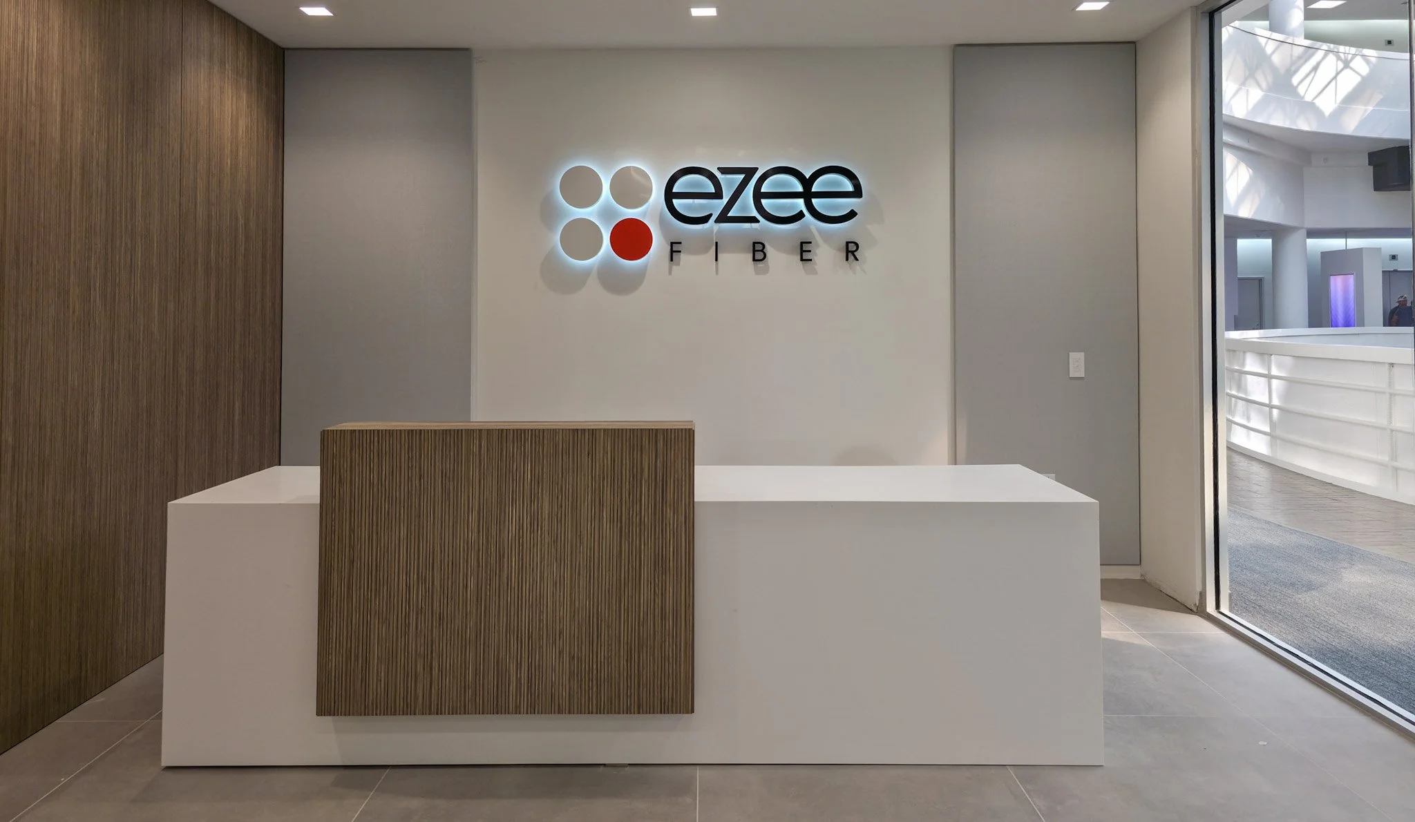Illuminated Ezee Fiber reception wall logo installed behind the front desk of a corporate office.