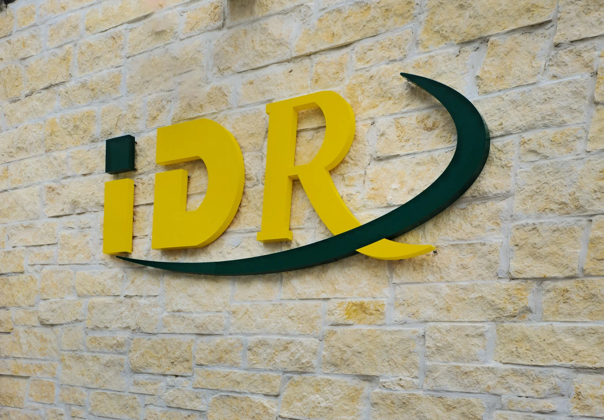 Dimensional exterior logo sign with painted acrylic letters mounted on a natural stone facade at a commercial building entrance.