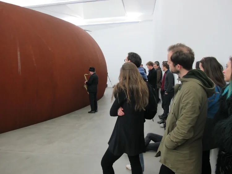 Intrigued audience members look and listen as Fefer explores the exterior of Serra's Backdoor Pipeline at Gagosian Gallery, London.