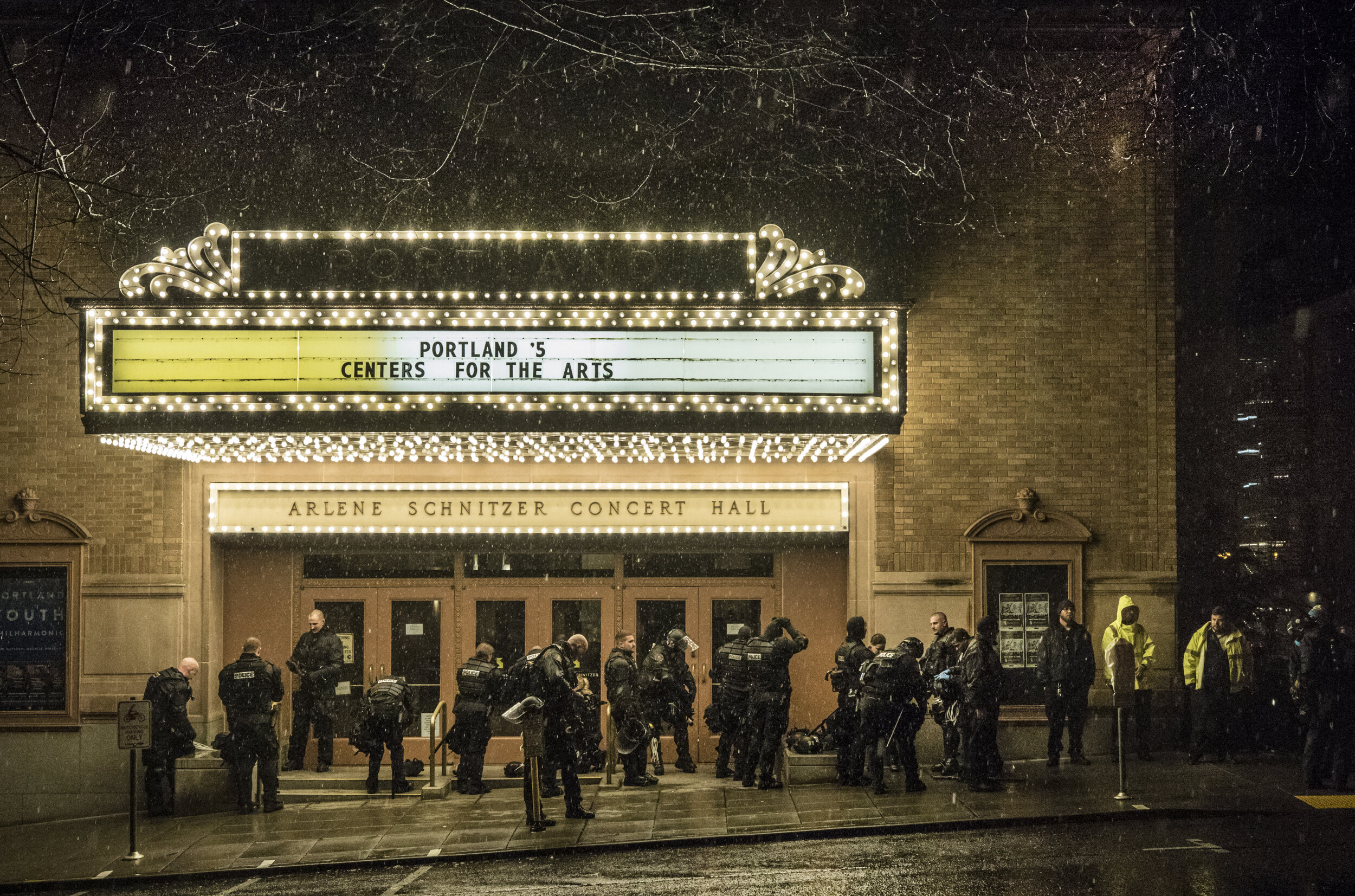After a long night of facing off against J20 protesters, Portland Police take a break from the rain underneath the marquee of the Arlene Schnitzer Concert Hall.