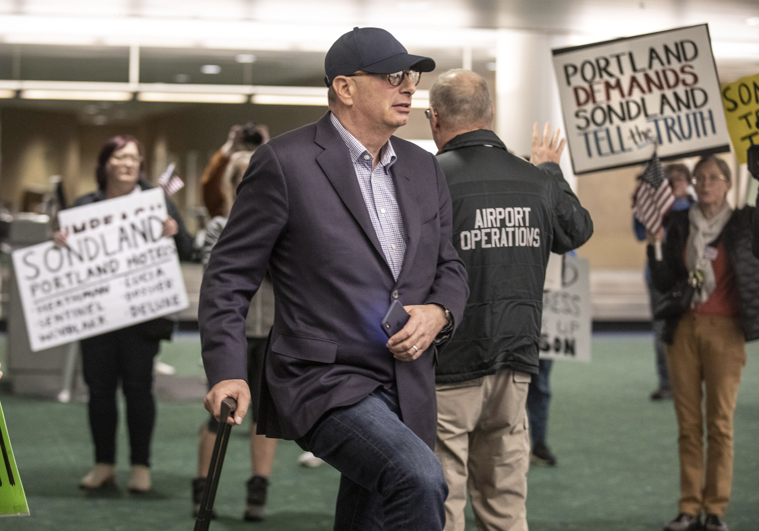 Portland hotelier and US diplomat Gordon Sondland waits for his luggage after arriving to protestors at Portland International Airport.