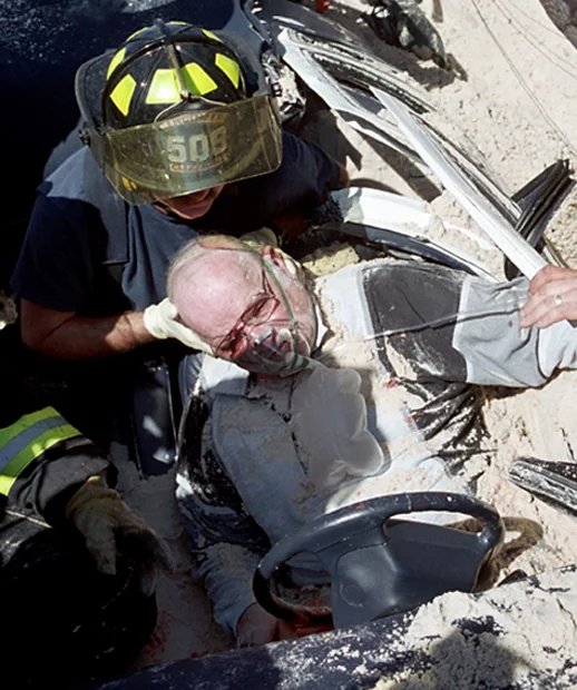  Clermont firefighters and bystanders work to remove a 63-year-old man from his car after a truck carrying sand overturned and crushed his car as he was waiting at an intersection. 