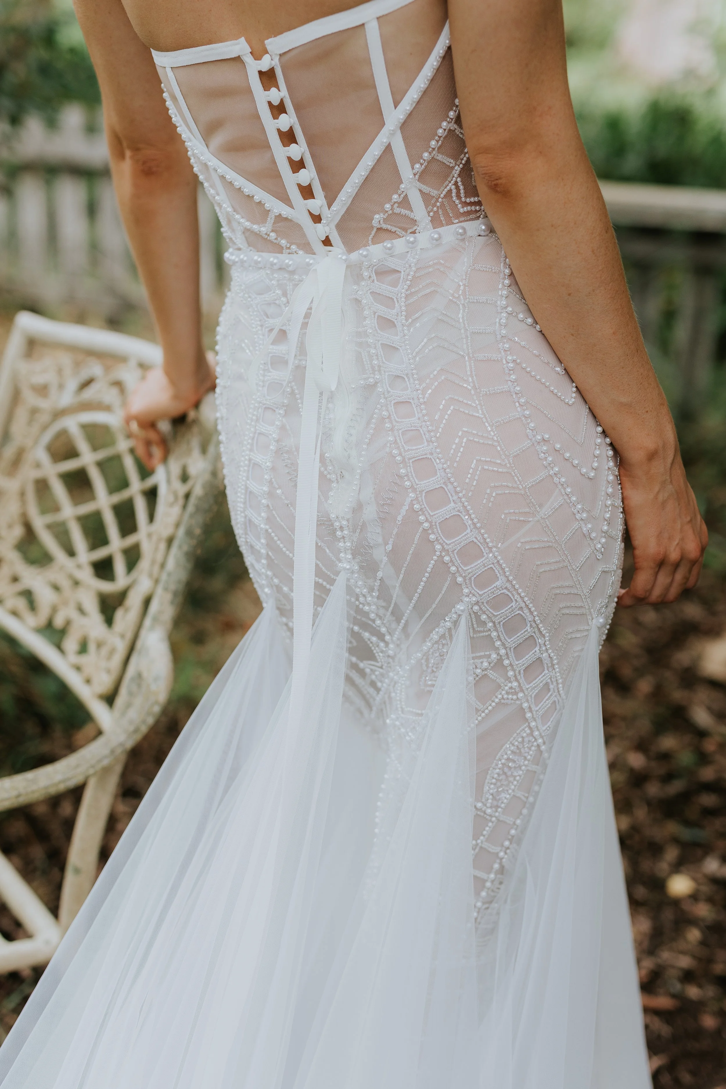 Close-up of a bride's wedding dress, featuring intricate beadwork and lace details, with a sheer back and ribbon tie.