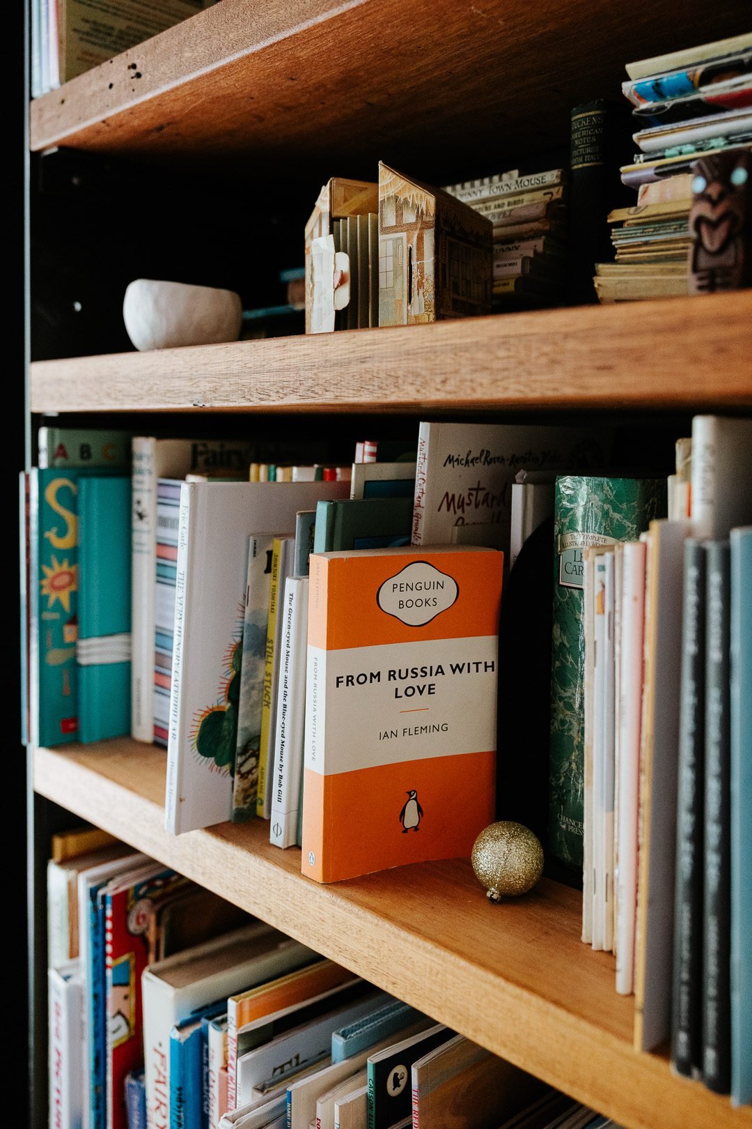 A bookshelf filled with various books, including 'From Russia With Love' by Ian Fleming, a small gold ornament, and other books with colorful covers.