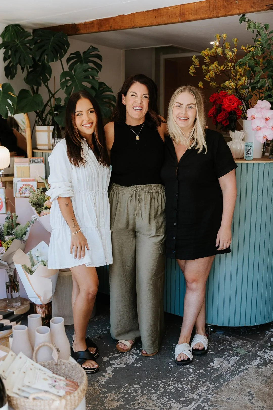 Branding Portraits for The Petal Sisters Florist on the Central Coast. Three women smiling and standing together in a flower shop, surrounded by plants, flowers, and decorative items.