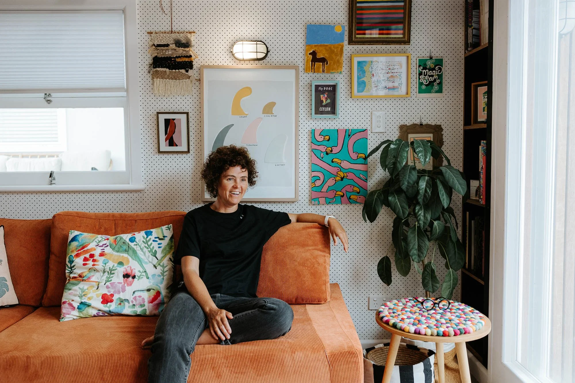 Portrait of Katherine Hall, owner and graphic designer Design and Opinion by Central Coast Branding Photographer. She is sitting on an orange couch, looking relaxed and natural and surrounded by artworks. Her studio was featured on Grand Designs