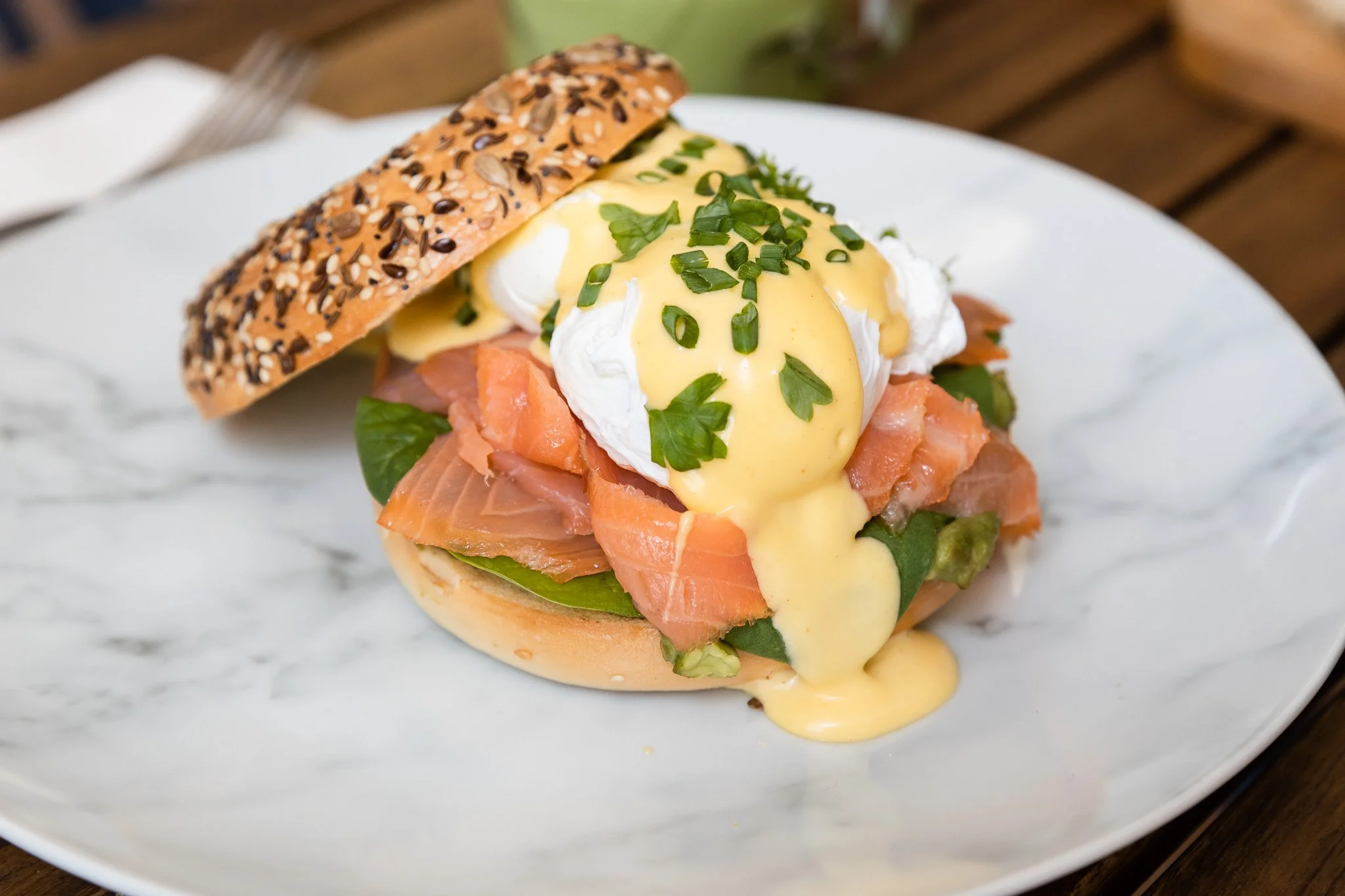 Smoked salmon eggs benedict on a toasted whole grain English muffin with hollandaise sauce, poached eggs, and garnished with chopped chives, served on a white plate.