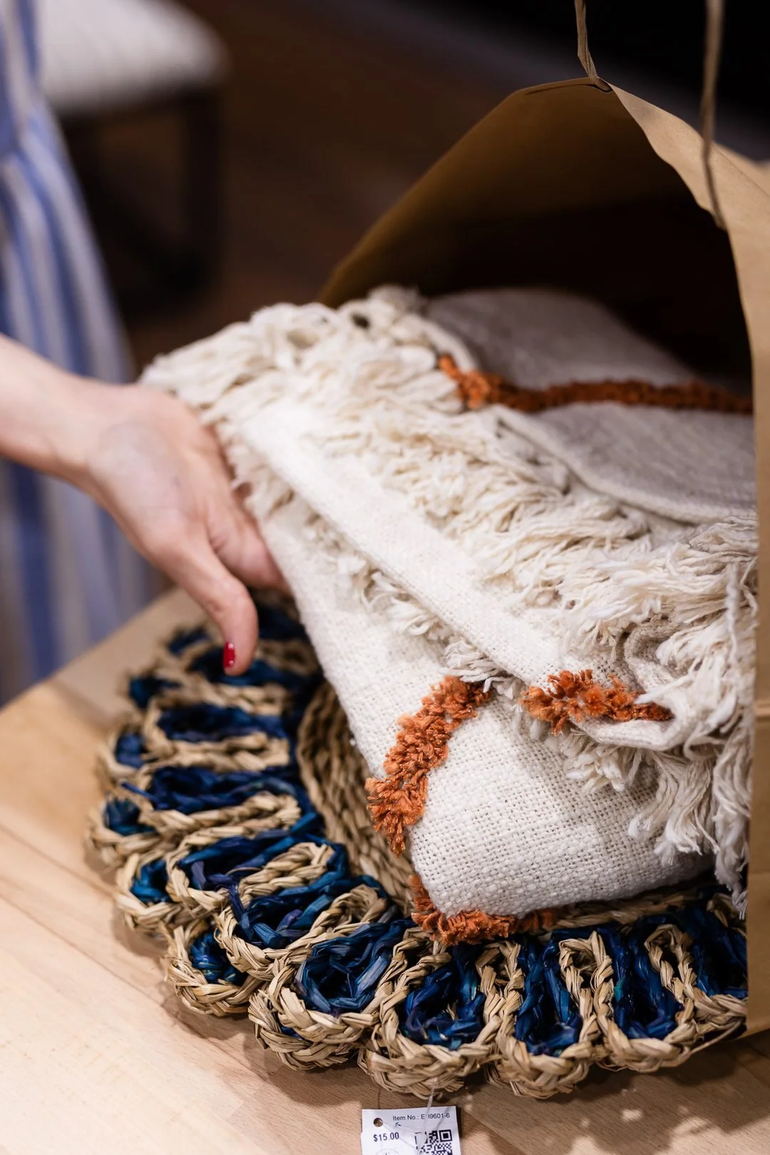 Hand folding a woven textile with loops, surrounded by other woven items in blue and natural fibers.