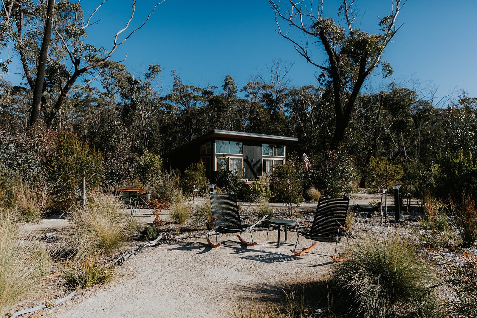 Boutique Accommodation Photography and Branding Sydney, Blue Mountains. Chates at Blackheath courtyard showing two rocking chairs side by side within a Australian bush landscape and a black chalet in the background