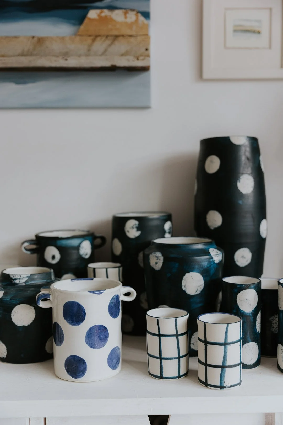 Collection of black and white ceramic vases and cups with polka dot and plaid patterns on a white surface.