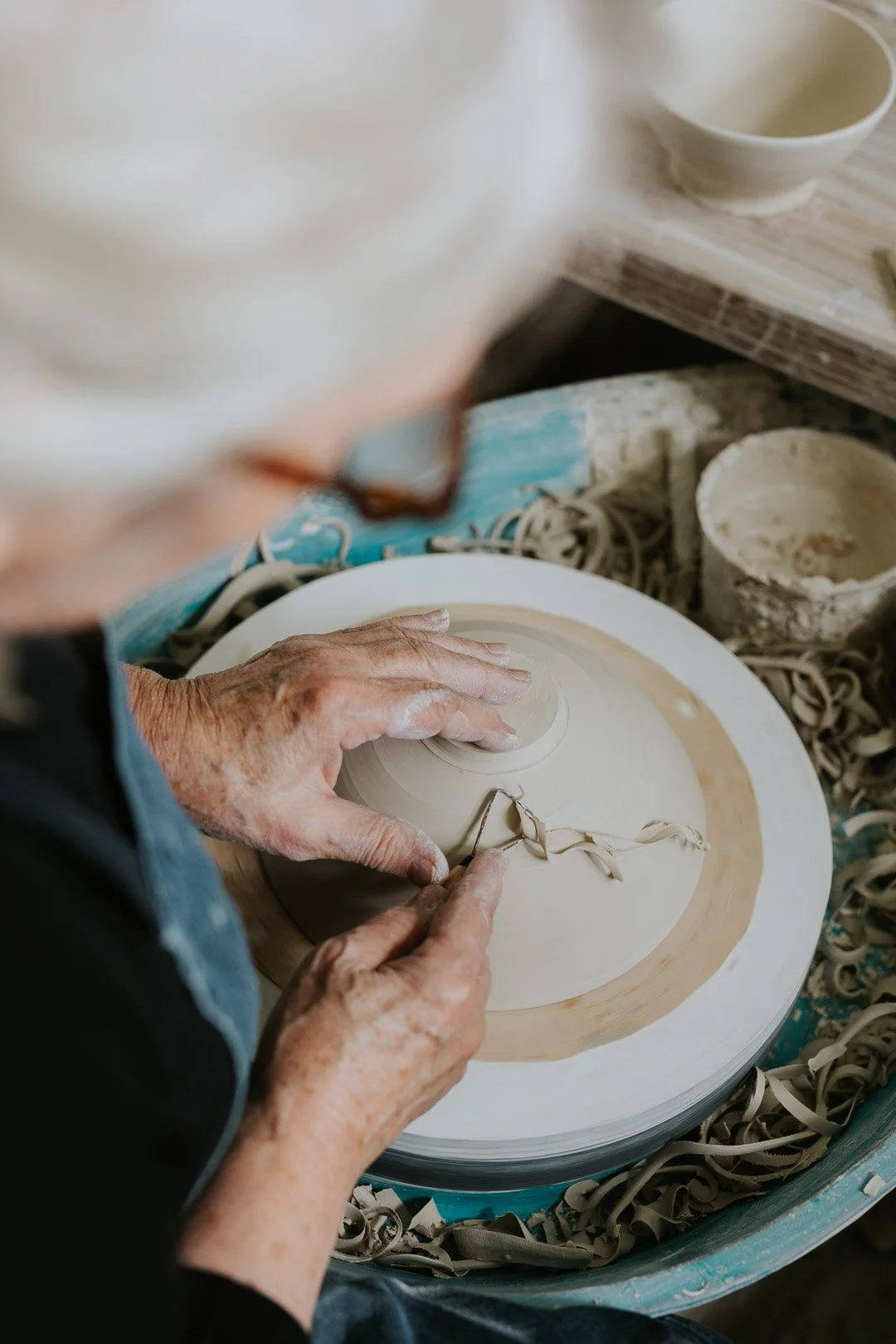 An elderly person shaping pottery on a spinning wheel in a pottery studio.