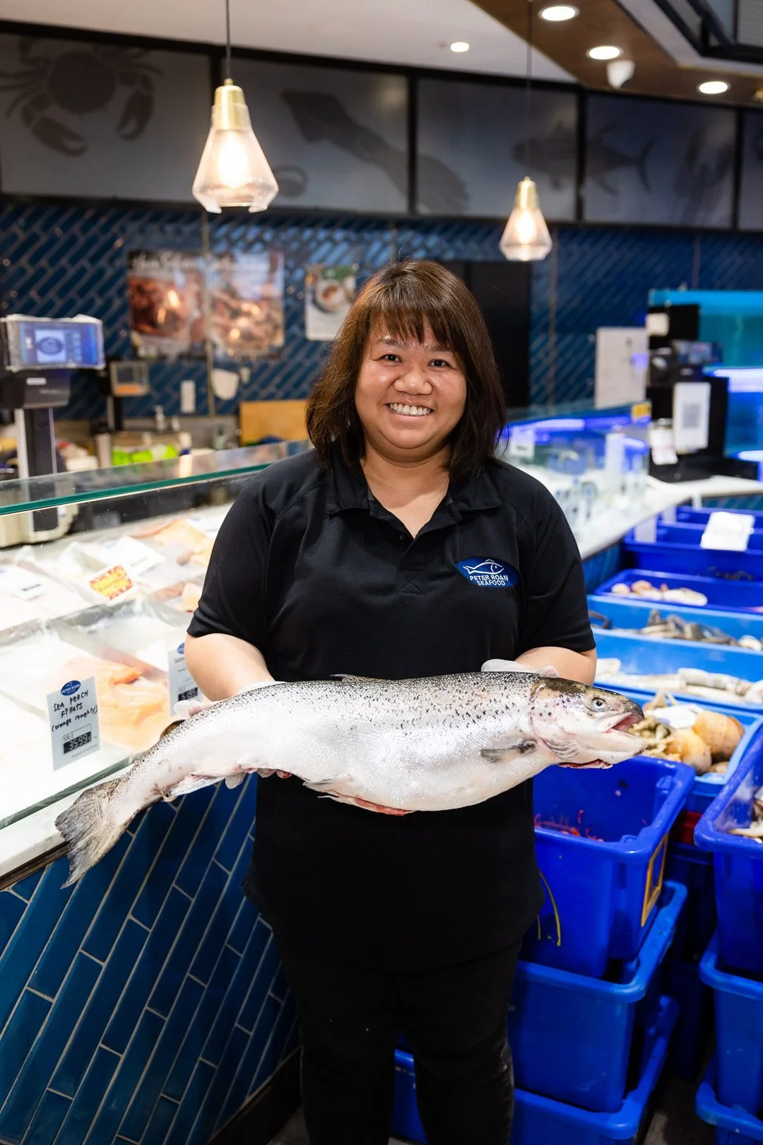 A woman smiling while holding a large fish inside a seafood market.