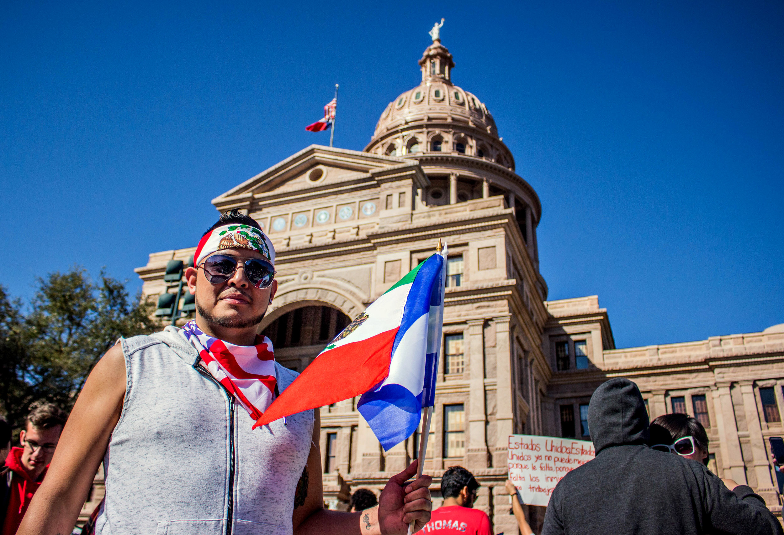 Victor Perez holds a Mexican flag, a Honduran flag, and wears an American flag around his neck in front of the Capitol.