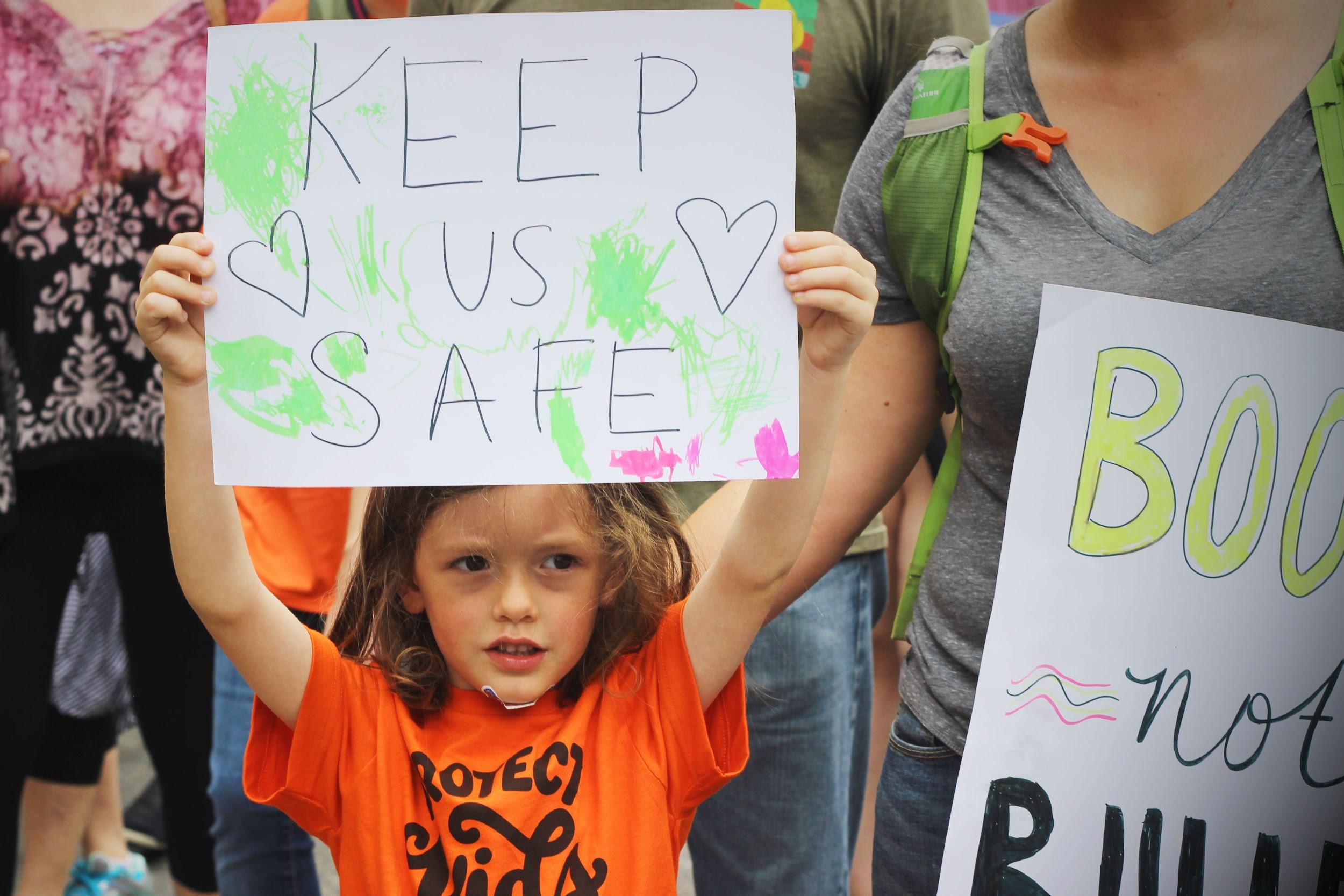 Standing alongside her mother, a young girl lifts up a sign.