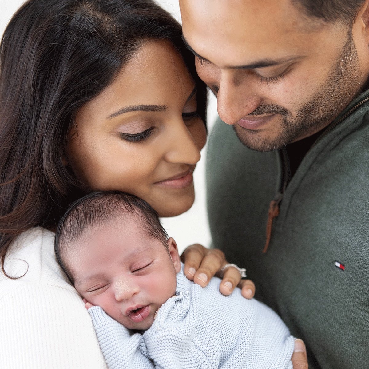 A loving couple gently holding their sleeping newborn baby, with their foreheads touching during a newborn photo shoot.