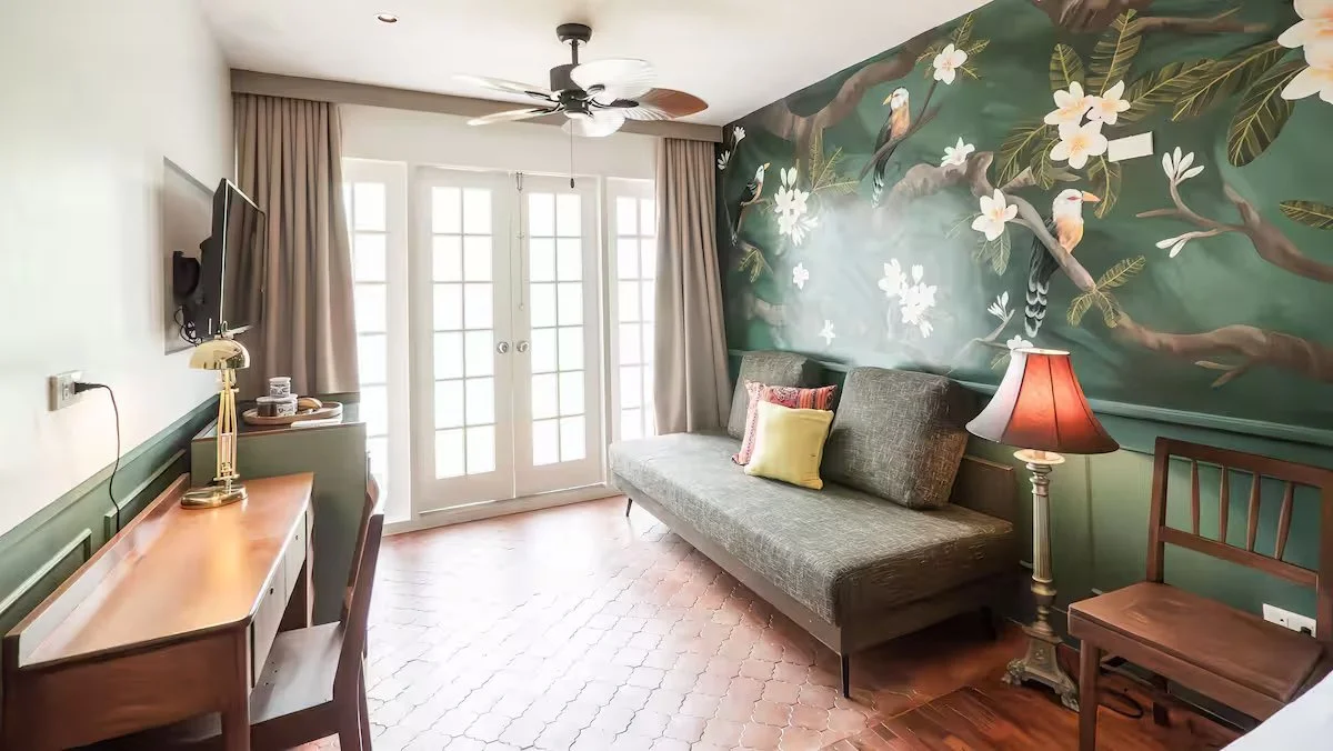 A bedroom for an airbnb located in a heritage property. Room has warm earth tones, with a dark green wall with a mural of a Kalachuchi plant and some aboloryo birds.