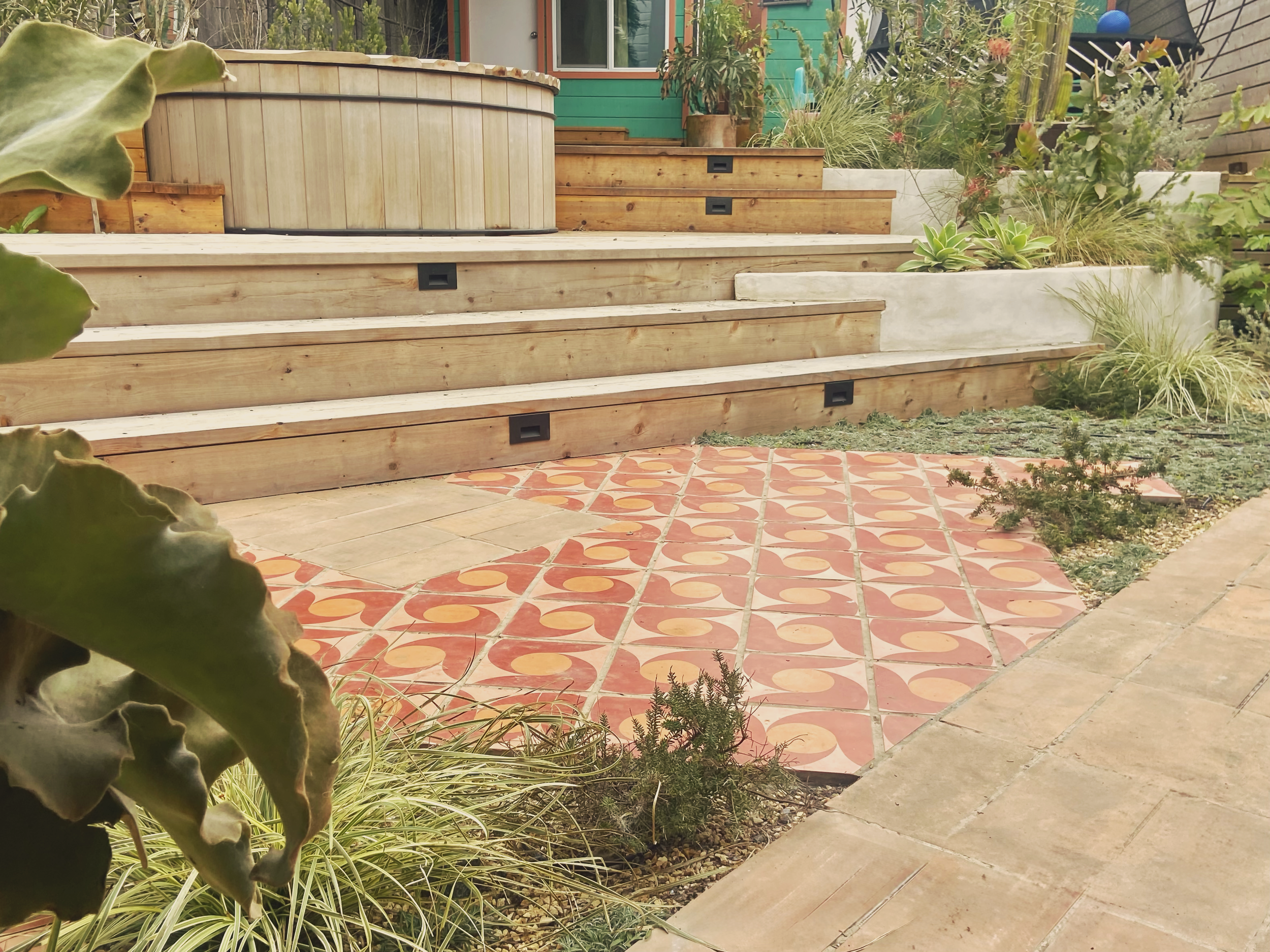 Backyard garden with wooden steps, potted plants, succulents, and patterned tile patio.