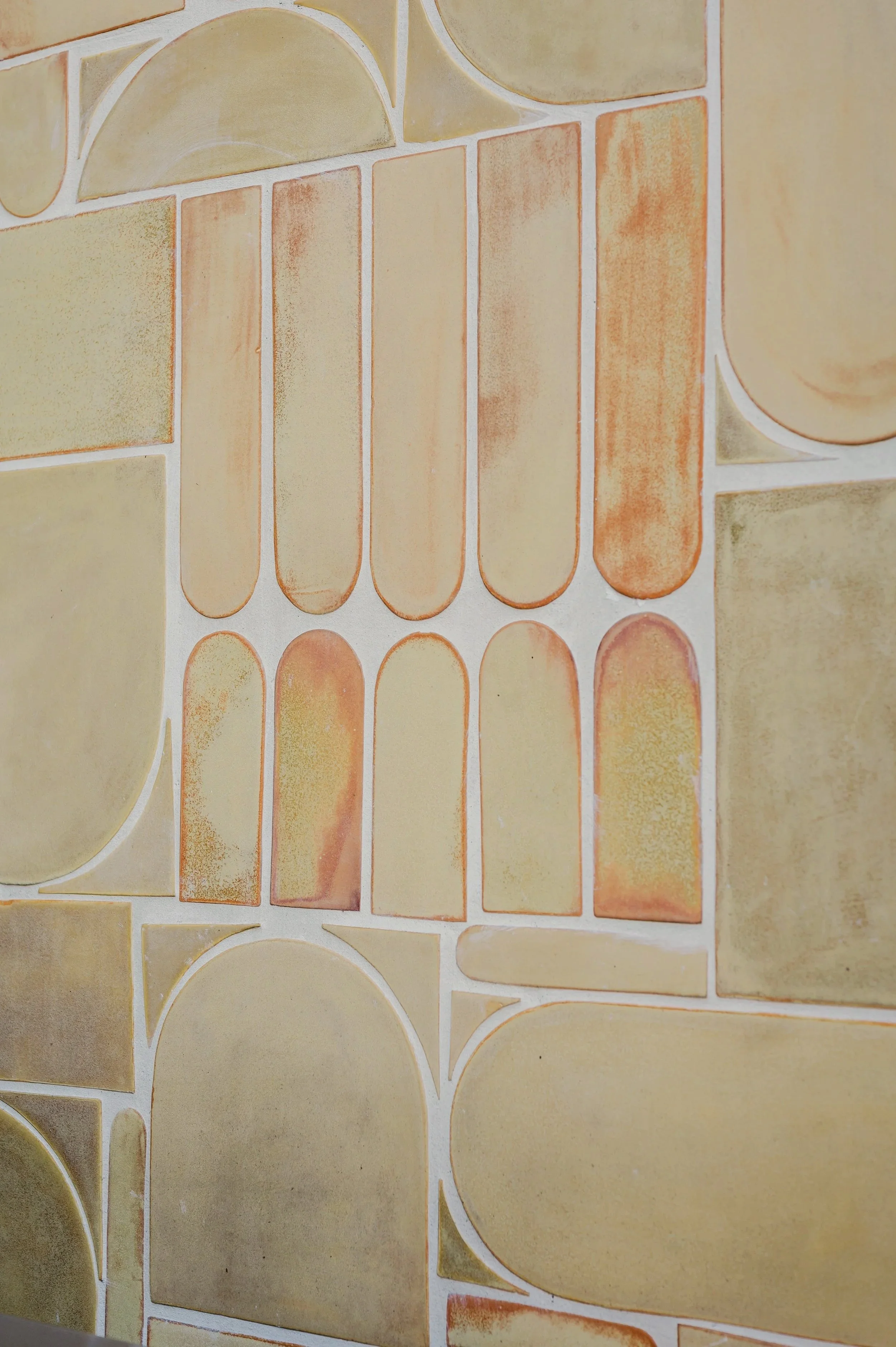 Close-up view of a wall decorated with beige and light brown tiles of various geometric shapes, including rectangles, squares, and semi-circles.